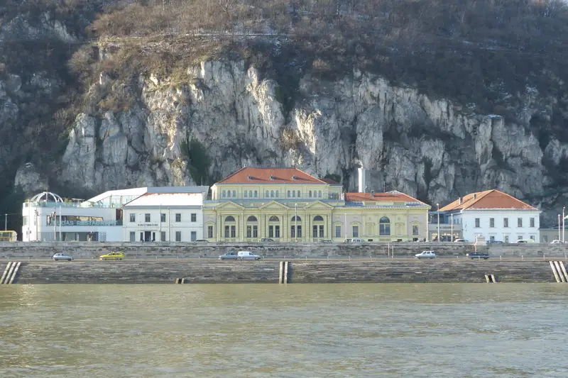 Façade néoclassique jaune et toits de tuiles rouges des bains Rudas, alignés le long du quai de Buda au pied de la falaise du mont Gellért, vus depuis l'autre rive du Danube par temps clair d'hiver.