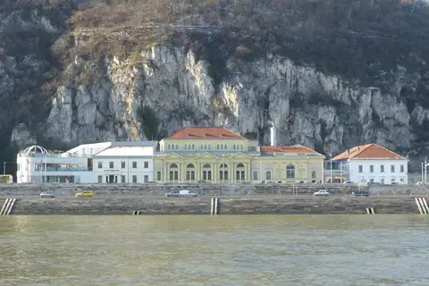 Façade néoclassique jaune et toits de tuiles rouges des bains Rudas, alignés le long du quai de Buda au pied de la falaise du mont Gellért, vus depuis l'autre rive du Danube par temps clair d'hiver.